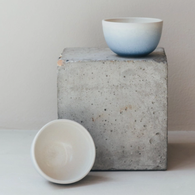 Duas tigelas de cerâmica, uma azul degradê e outra branca, sobre bloco de cimento cinzento