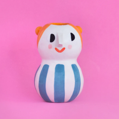vaso cerâmico decorativo pintado à mão com padrão riscas azuis e brancas e rosto estilizado sobre fundo rosa