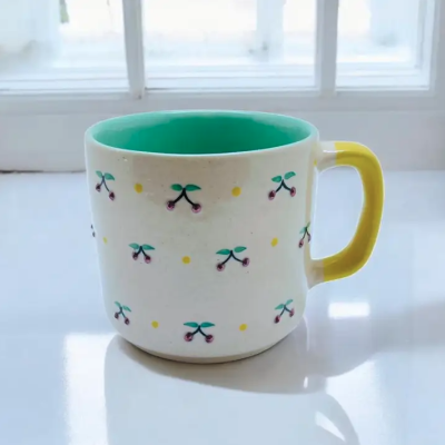 Caneca de cerâmica branca com padrão de cerejas e pega amarela