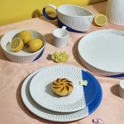 Conjunto de louça de cerâmica azul e branca com limões e flores sobre mesa rosa claro