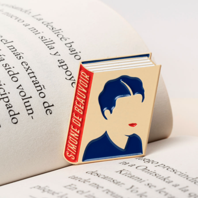 Marcador de livros metálico com desenho de rosto feminino e texto 'Simone de Beauvoir'