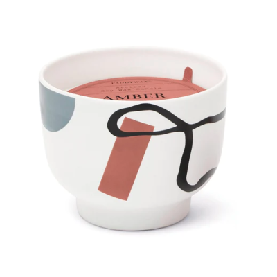 Vela perfumada em pote cerâmico branco com padrões abstratos e etiqueta laranja