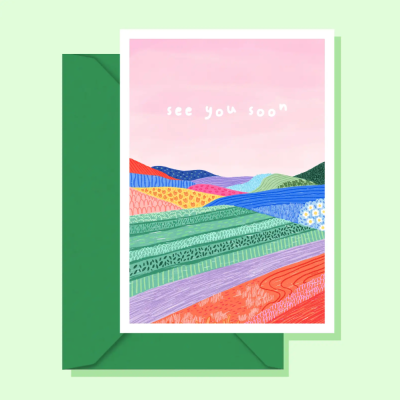 Cartão colorido com ilustração de campos e colinas e texto see you soon com envelope verde