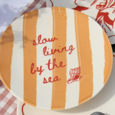 Prato redondo com riscas laranjas e creme com texto em vermelho e desenho de concha