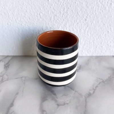 Caneca cerâmica riscas pretas e brancas com interior laranja num fundo branco e superfície de mármore cinzento.