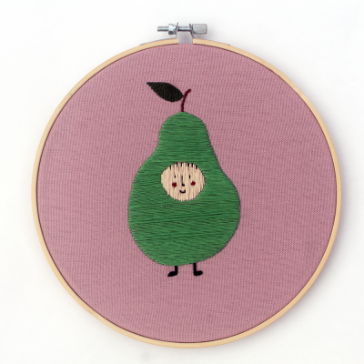 Bordado de pêra verde com rosto sorridente em aro de madeira com fundo cor de rosa