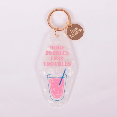 Chaveiro transparente com texto rosa e pendente dourado ao fundo branco
