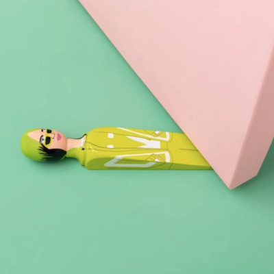 Boneco decorativo com cabeça pintada e corpo amarelo com linhas brancas sobre fundo verde claro