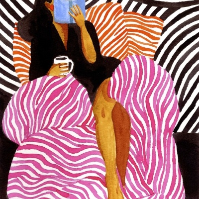 Mulher sentada com manta rosa e branco, almofadas laranja e branco, lendo um livro azul e segurando uma chávena branca