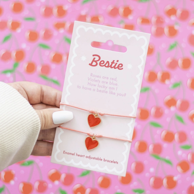 Pulseiras ajustáveis com corações vermelhos em cartão 'Bestie' sobre fundo de cerejas