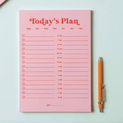 Bloco rosa com plano diário e caneta laranja ao lado