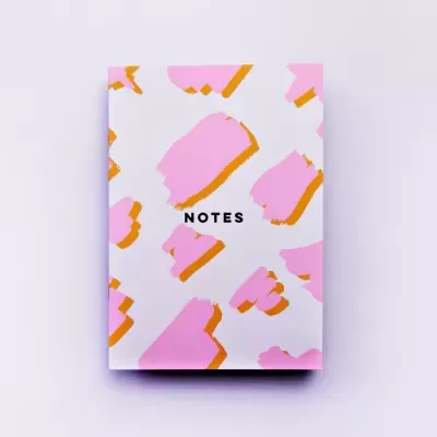 Caderno branco com manchas rosa e laranja e texto 'NOTES'