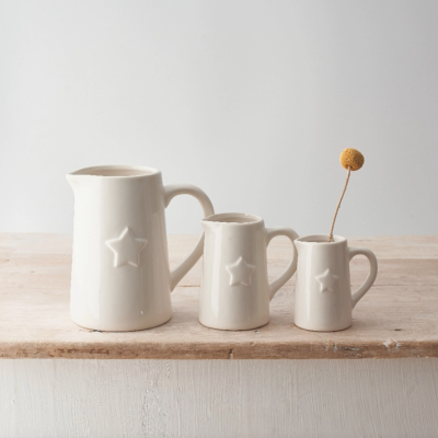 Três jarros de cerâmica branca com estrelas em relevo numa superfície de madeira clara