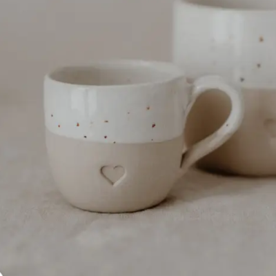 Caneca de cerâmica branca e bege com coração recortado e pontos castanhos