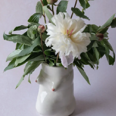 Vaso cerâmico branco com design de rosto feminino e flores brancas