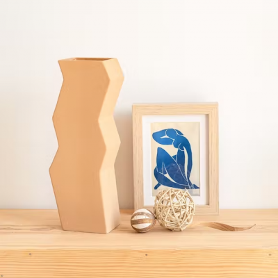 Vaso cerâmico bege, quadro de figura azul em moldura de madeira, duas bolas decorativas sobre madeira clara