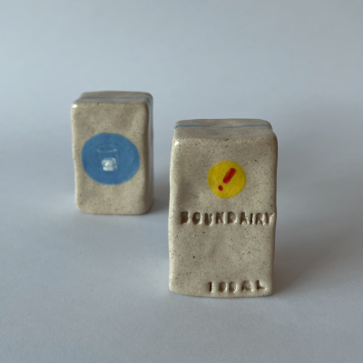 Dois pequenos blocos cerâmicos retangulares cinzentos com círculos coloridos e texto em relevo