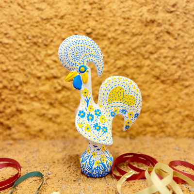 Estatueta de galo em cerâmica azul e amarelo com fitas coloridas no chão