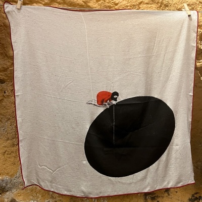 Manta bege com borda vermelha e estampa de menina ajoelhada a olhar para círculo preto