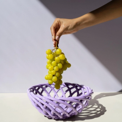 Tigela lilás trançada com cacho de uvas verdes segurado por uma mão
