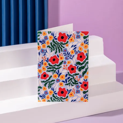 Cartão dobrado com padrão floral colorido em degraus brancos contra fundo lilás e azul.