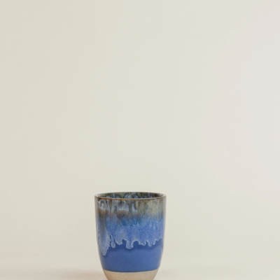Copo cerâmico azul com acabamento em tons de azul e verde em fundo neutro