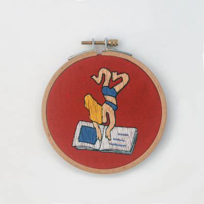 Bordado colorido em bastidor de madeira mostrando pessoa invertida em prancha sobre fundo vermelho