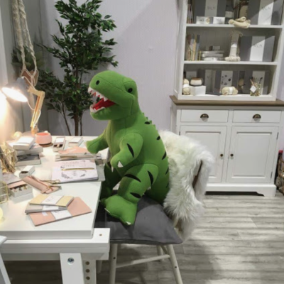 Boneco de peluche dinossauro verde sentado em cadeira junto a secretária branca num quarto