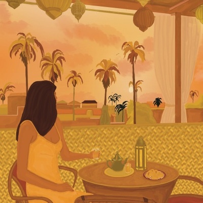 Mulher de vestido amarelo sentada numa varanda com mesa de chá e palmeiras ao pôr do sol