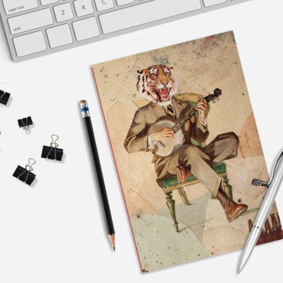 Caderno ilustrado com homem com cabeça de tigre a tocar banjo, lápis preto, caneta prateada, clips negros e teclado branco.