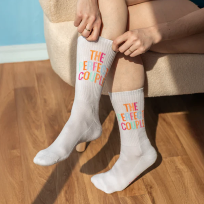 Meias brancas com texto colorido THE PERFECT COUPLE usadas por pessoa sentada