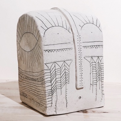 Objeto de cerâmica branca com desenhos geométricos pretos em superfície de madeira clara