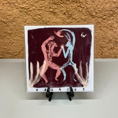 Azulejo decorativo com duas figuras estilizadas a dançar sobre fundo castanho escuro e texto ABRAÇOS