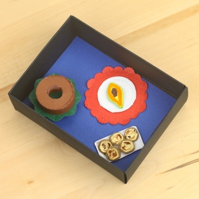 Miniaturas de papel representando comida dentro de uma caixa preta com interior azul