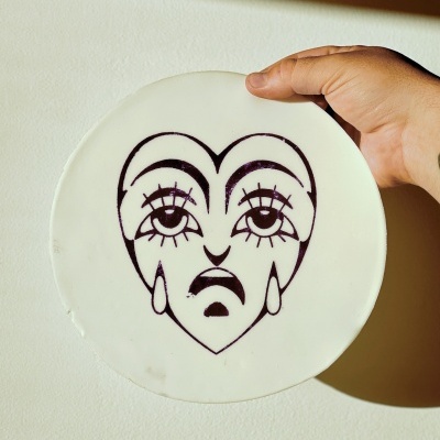 Disco branco com rosto triste desenhado em preto sendo segurado por uma mão