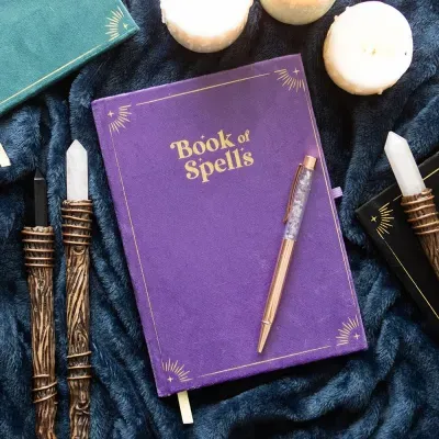 Livro Book of Spells roxo com caneta, velas e varinhas em tecido azul escuro