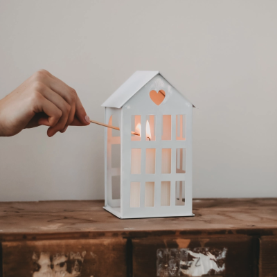 Lanterna branca em forma de casa com vela acesa dentro em móvel de madeira