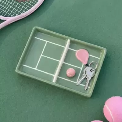 Tabuleiro cerâmico verde com padrão de campo de ténis e bola rosa com porta-chaves em forma de raquete cor-de-rosa, com raquete e bolas de ténis cor-de-rosa ao lado
