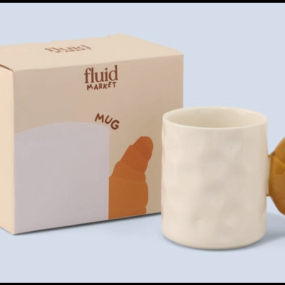 Caneca branca com pega em forma de croissant e embalagem ao lado