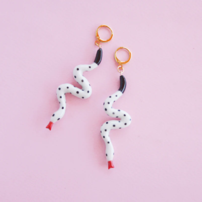 Brincos de serpente brancos com pontos pretos em fundo rosa