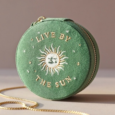 Bolsa redonda verde com bordado de sol e texto LIVE BY THE SUN