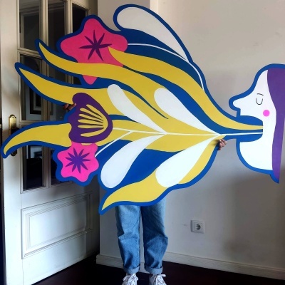 Cartaz grande colorido com personagem e flores abstratas segurado por pessoa em interior