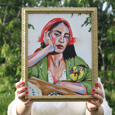 Pintura de mulher com lenço vermelho e pássaro amarelo em moldura dourada a ser segurada ao ar livre