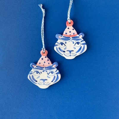 Dois ornamentos em forma de cabeça de tigre com padrão azul e branco e chapéu rosa