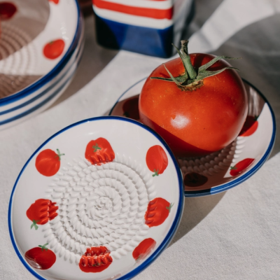 Pratos cerâmicos pequenos com estampas de tomate e textura de ralar sobre mesa com tomate e embalagem ao fundo