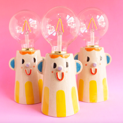Três candeeiros de mesa com base sorridente colorida e lâmpadas redondas