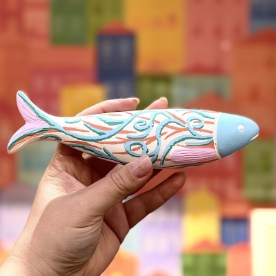 Peixe de madeira pintado à mão com padrões ondulados coloridos segurado por uma mão