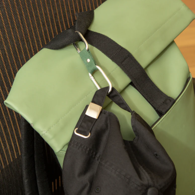 Mochila verde pendurada numa cadeira de escritório preta, com um boné preto preso ao mosquetão