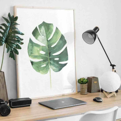 Secretária de madeira com laptop, candeeiro, quadro de folha verde e planta