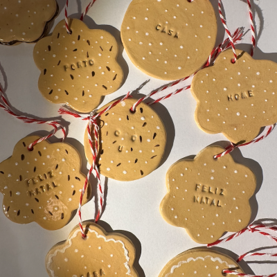 Ornamentos decorativos em forma de bolachas com frases em português e inglês pendurados por fios vermelhos e brancos